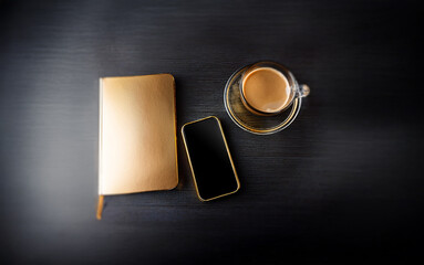 Wall Mural - A gold notebook, smartphone, and a glass cup of coffee on a dark wooden surface.