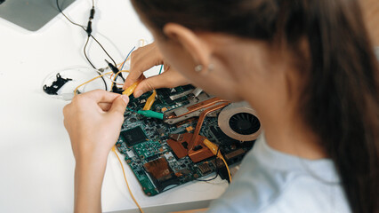 Top view of young highschool girl fixing mainboard at STEM technology class. Closeup of caucasian student wear casual cloth by using wire and electronic equipment to repair mother board. Edification.