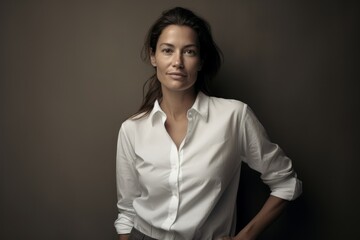 Portrait of a satisfied woman in her 40s wearing a simple cotton shirt in bare monochromatic room