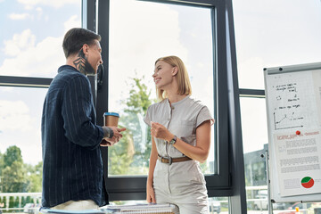 Two coworkers enjoy a lively discussion while standing in a modern office filled with natural light.