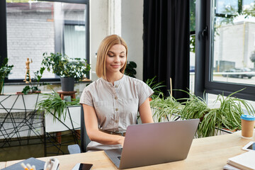 A young professional enjoys working on a laptop in a lively green office environment.