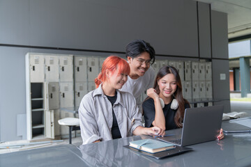 Three young university students are collaborating on a project, engaging with a laptop in a university hallway with lockers in the background, showcasing teamwork and modern education