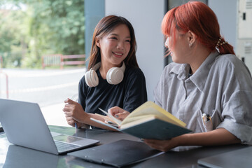 two young female students collaborating on a project, discussing and using a laptop in a modern lear