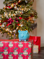 Blue piggy bank front of a Christmas tree decorated with beautiful Christmas vibes. Holiday season in December for family and friends together and give a gift and using money. saving money for present