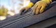 © BrilliantPixels - Close-Up of a Gloved Hand Installing Asphalt Shingles on a Roof, with a Shallow Depth of Field and Blurred Background