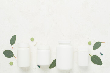 Wall Mural - Bottles with pills and green leaves on concrete background, top view