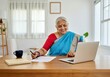 © Anna - Smiling elderly Indian woman in traditional attire working on laptop at home office desk