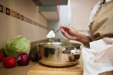 Close-up of cooking ingredients and hand stirring pot in kitchen