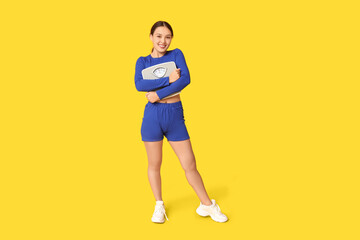 Poster - Young woman in sportswear and with weight scales on yellow background. Slimming concept