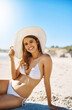 © peopleimages.com - Woman, portrait and hat on beach for holiday, vacation and summer adventure by ocean outdoor. Tourist, sun accessory and Miami for smile, confidence and weekend travel with swimsuit for happiness