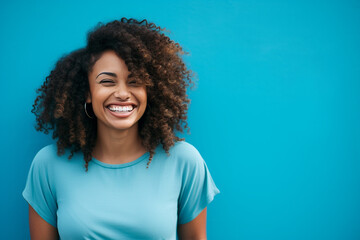 beautiful young black woman smiling and standing in front of a blue wall with copy space to the righ