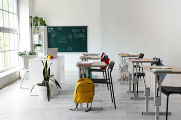 Wall Mural - Interior of empty classroom with school desks and text BACK TO SCHOOL on chalkboard