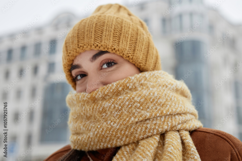 Close up portrait of cute girl wearing knit hat in winter and wrapped in scarf looking at camera with big hazel eyes copy space