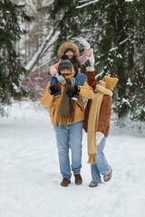 Wall Mural - Vertical full length portrait of playful young family walking together in winter forest with father carrying smiling little girl on shoulders