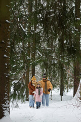 Wall Mural - Vertical wide angle view of happy young family walking towards camera in beautiful winter forest with tall trees all smiling enjoying day together copy space