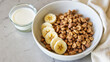 © Tameem - A bowl of granola with bananas and milk, resting on a table.