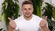 © Aris Suwanmalee - A confident man gives a thumbs up, showcasing positivity and approval in a bright indoor setting surrounded by greenery.