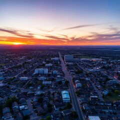 Aerial cityscape view, dramatic sunset sky, vibrant orange and pink clouds, urban sprawl, long straight road, dusk lighting, bird's eye perspective, twilight atmosphere, geometric city layout, horizon