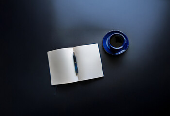 Aufkleber - an open notebook with a pen lies next to a cup of coffee on a dark surface.