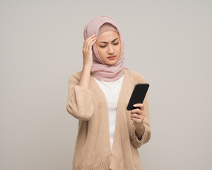 Unhappy young asian muslim woman holding smartphone standing on isolated white background. Feeling stressed Muslim woman wearing abaya and hijab fashion costume shot in studio