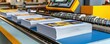 © WACHI - A printing machine displays stacks of colorful printed materials ready for processing in a modern production environment.