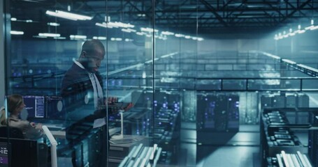 Poster - Black Male Infrastructure Architect Reviewing Virtualization Strategies on a Laptop Computer, Standing in Office Next to Towering Racks of Servers, Planning to Scale Client Cloud Solutions