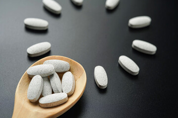 white Pills Medicine tablet capsules in a wooden spoon blister pack on a black background