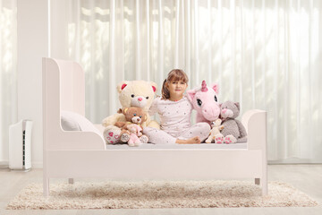 Poster - Girl in pajamas sitting in bed with her soft toys