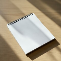 Blank spiral notebook on a wooden desk partially illuminated by sunlight.