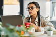 © Bliss - A professional young woman sips coffee while focused on her laptop, immersed in her work.