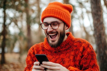 Poster - A man in an orange sweater and beanie looks at his cell phone with a smile