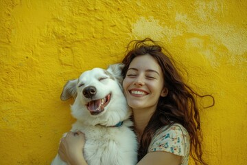 A woman holds a small white dog in front of a bright yellow wall