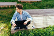 © Iryna - Young Caucasian adult male sitting cross-legged outdoors by small wind turbine model.