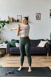 © Bliss - A young woman in crop top and leggings stretches her arm while practicing at home in the morning.