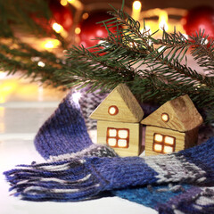 two houses with light in the window wrapped in a scarf against the background of a Christmas tree and garland lights. warm winter holidays at home