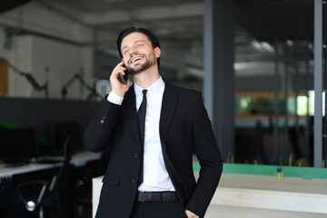 A man in a suit is talking on his cell phone. He is smiling and he is enjoying the conversation