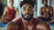 © JoxyAimages - A focused individual in a red tank top participates in a yoga class, showcasing strength and concentration. The setting is professional and tranquil with others in background.