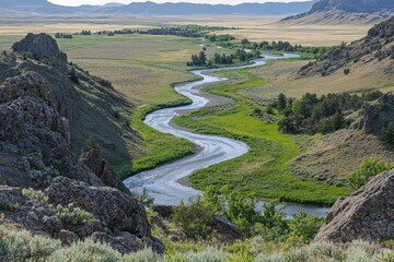 Poster - A winding river meandering through a valley surrounded by rocky hills and lush vegetation.