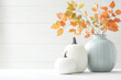 © KDesign - serene autumn arrangement featuring white pumpkins and blue vase with orange leaves, evoking cozy seasonal atmosphere