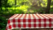 © Rangga Bimantara - A red and white checkered tablecloth drapes over a wooden table, set against a blurred green forest background, suggesting a picnic setting.