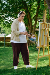 A creative person paints joyfully under trees, wearing headphones and a bright smile.