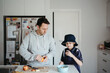© Austockphoto - man cutting fruits on the kitchen counter with young boy beside him getting ready for school