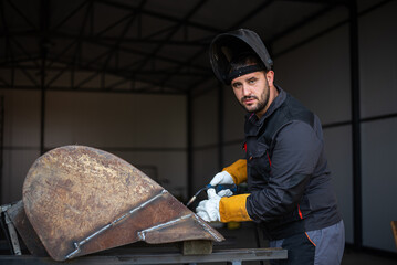 Metal worker welding metal part in workshop