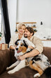 © LIGHTFIELD STUDIOS - A happy couple sits closely together on a sofa with their affectionate dog in a warm living room.