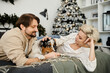 © LIGHTFIELD STUDIOS - A couple enjoys a warm moment on the couch with their dog, decorated for the holidays.