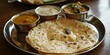 © StockUp - Traditional Indian naan served with curries and condiments on a classic silver platter.