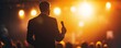 © Cheewynn - Keynote speaker in suit, microphone in hand, stage spotlight, engaging with audience, dynamic lighting, inspirational speech scene, business event