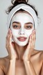 © Natalya - Young woman with facial mask smiling and applying skincare in a beauty routine at home