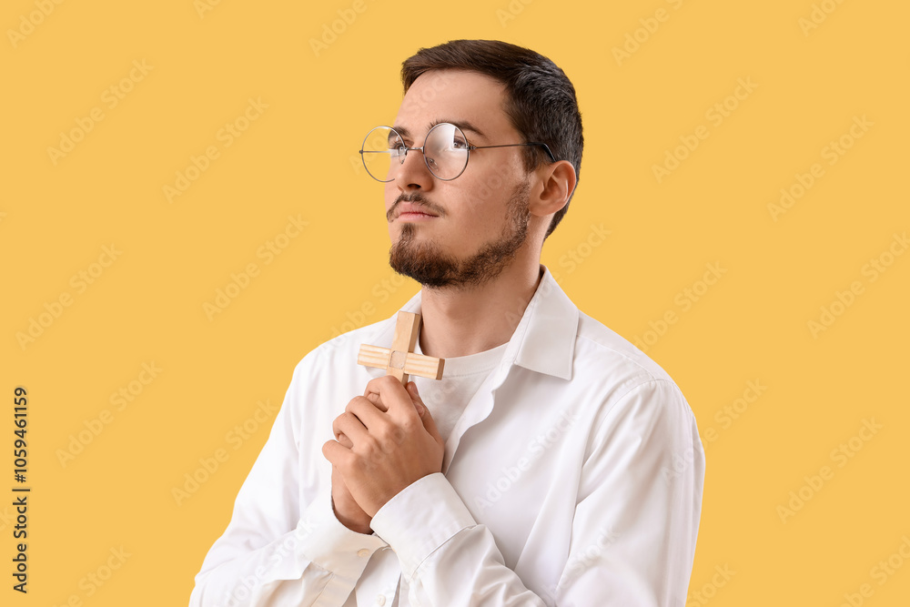 Young man with wooden cross praying on yellow background