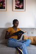 © Milles Studio/Stocksy - Positive young woman reading book on couch at home